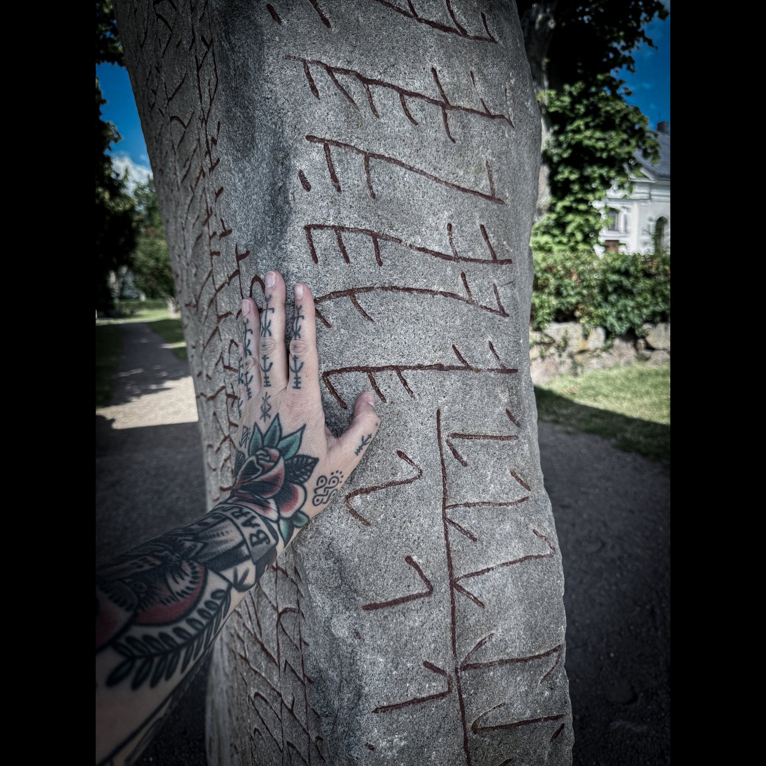 Hand of Hélène Morrigan touching a Swedish runestone carved with red Younger Futhark runes and bindrunes