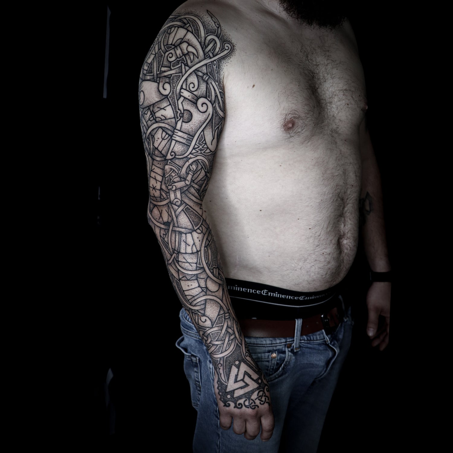 Nordic mythology full sleeve tattoo depicting the sacrifice of Tyr with Fenrir across the arm, Valknut on the hand and Younger Futhark runic inscriptions integrated into the design