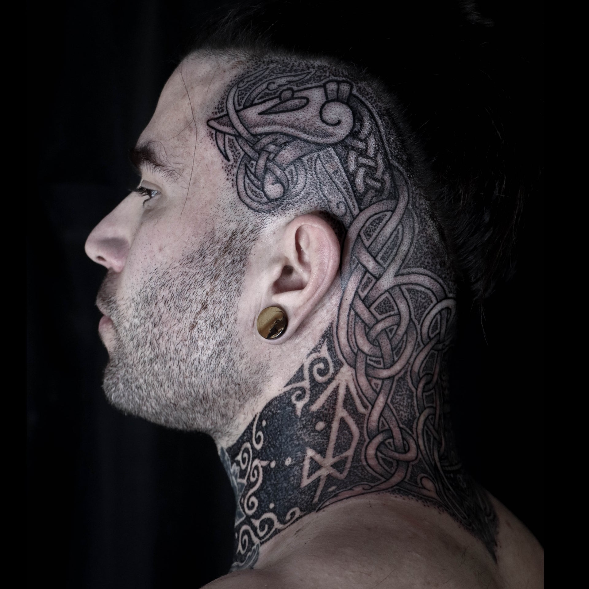 Norse head tattoo depicting a serpent with interlaced knotwork and bindrunes in blackwork style