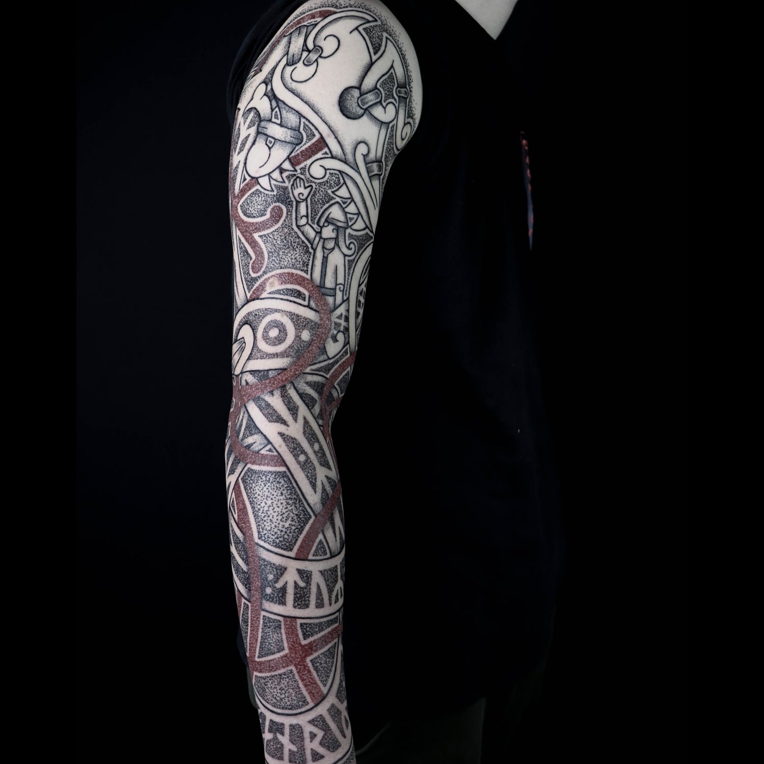 Norse full sleeve tattoo depicting the nordic mythology sacrifice of Tyr with Fenrir across the arm, featuring Younger Futhark runic inscriptions and red interlaced knotwork details