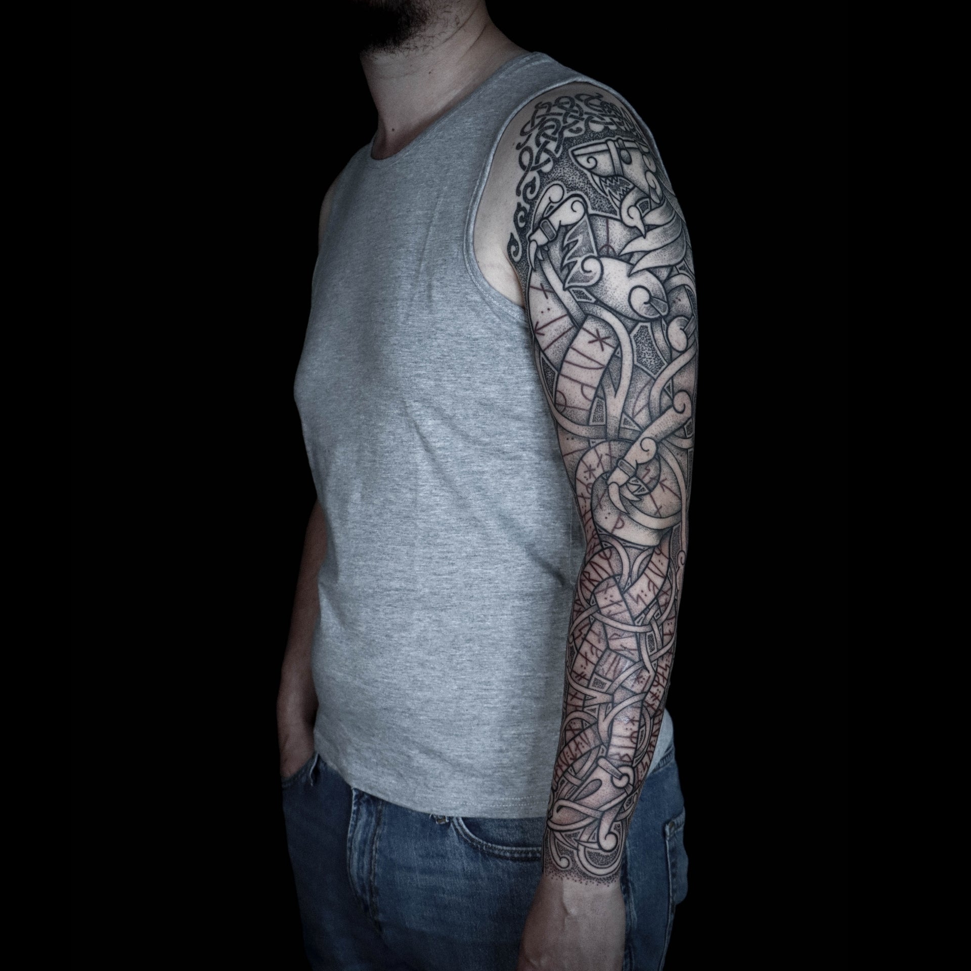 Scandinavian full sleeve tattoo featuring a Nordic-style lion above Jormungandr with red runic inscriptions in Younger Futhark integrated into interlaced knotwork composition