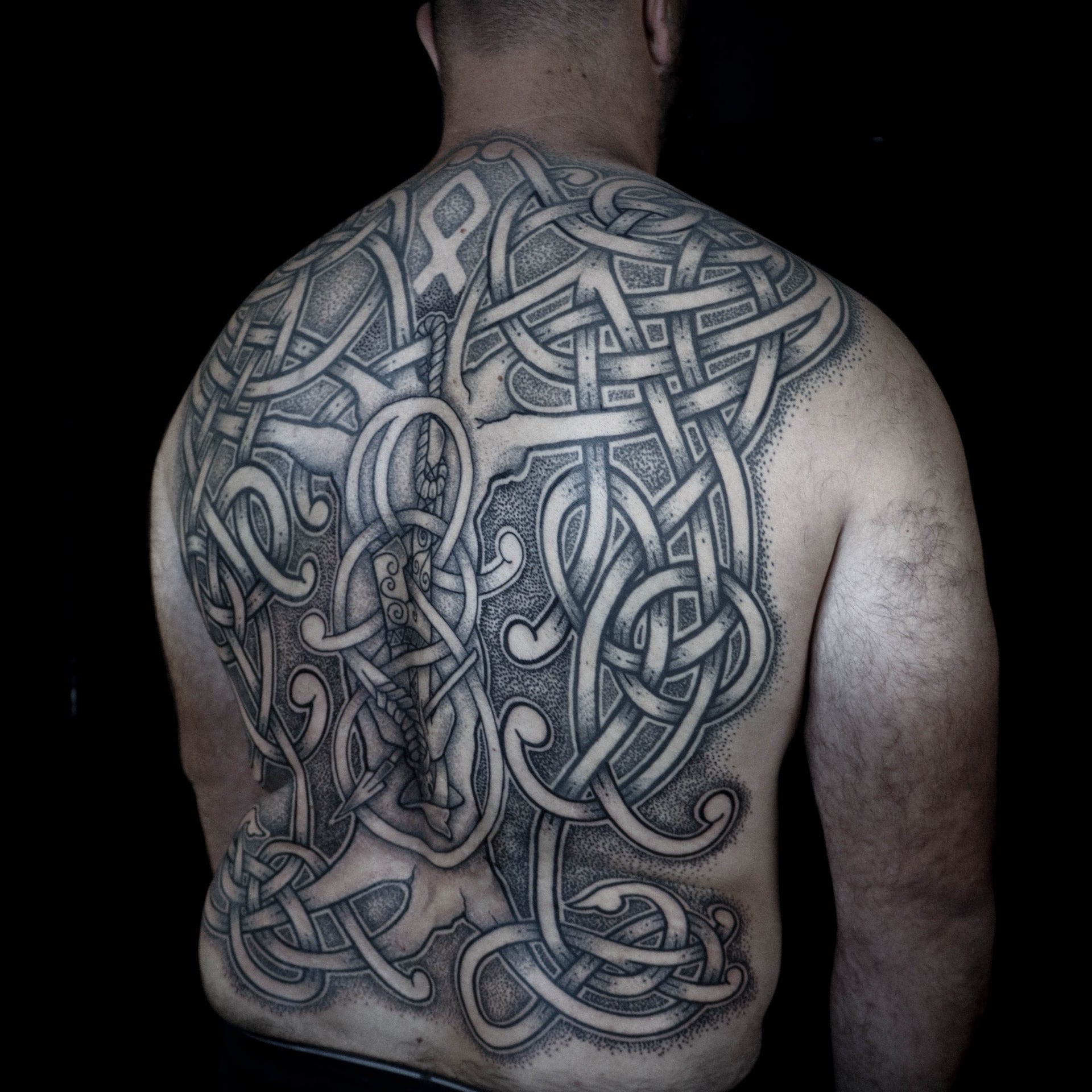 Scandinavian backpiece tattoo of Odin hanging from Yggdrasil with a spear through his chest and Othala rune above, composed in intricate knotwork style