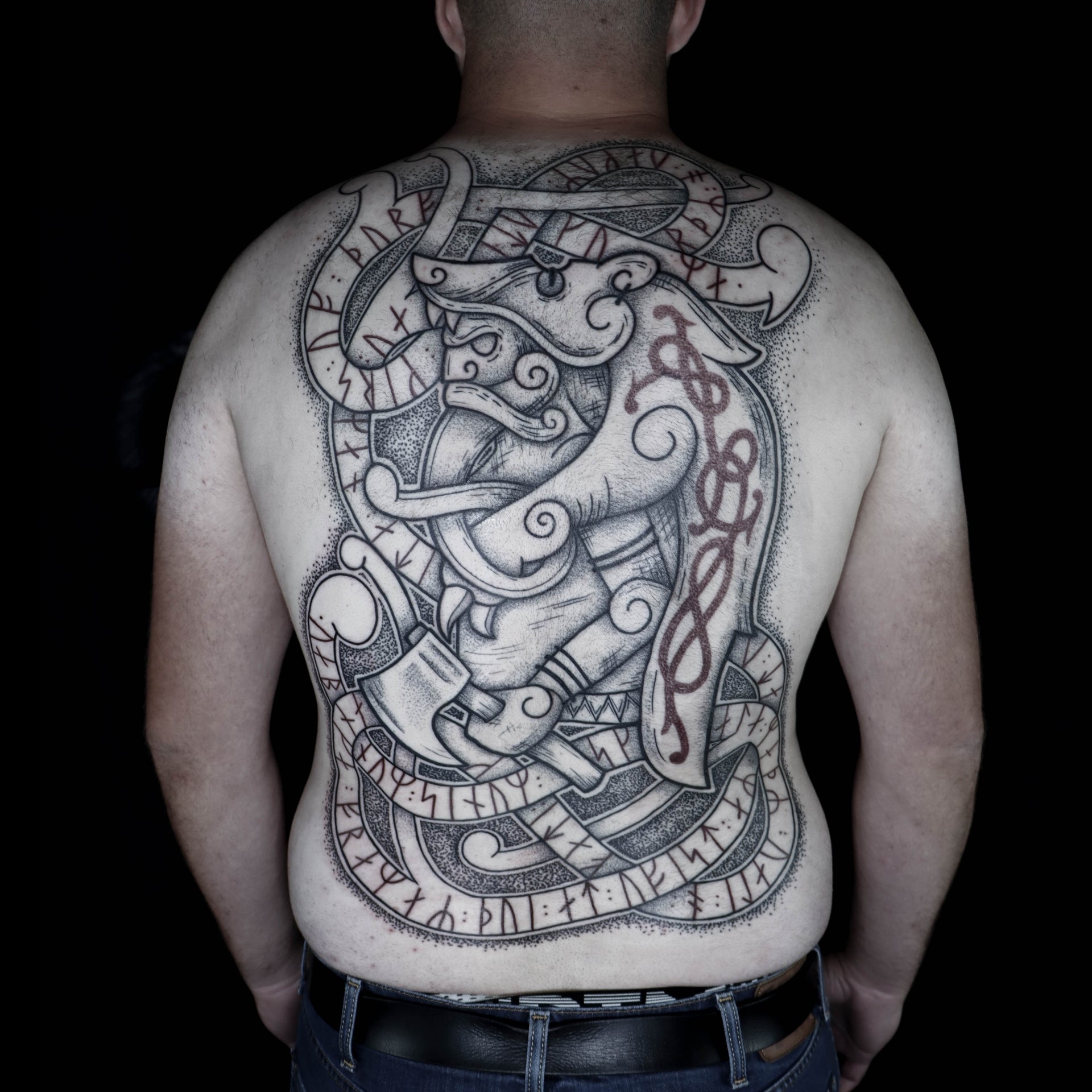 Viking backpiece tattoo featuring a large berserker with red Younger Futhark runic stanza woven into interlaced knotwork and subtle red ornamental details