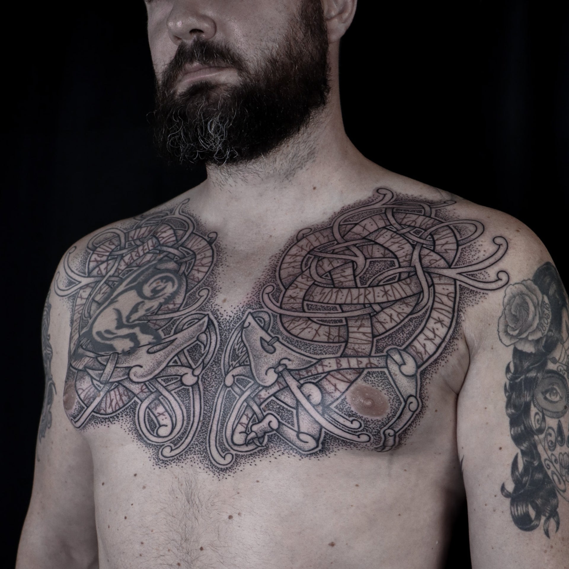 Viking chest tattoo featuring Fenrir and Jormungandr with red runic stenza from the Hávamál woven into intricate knotwork design