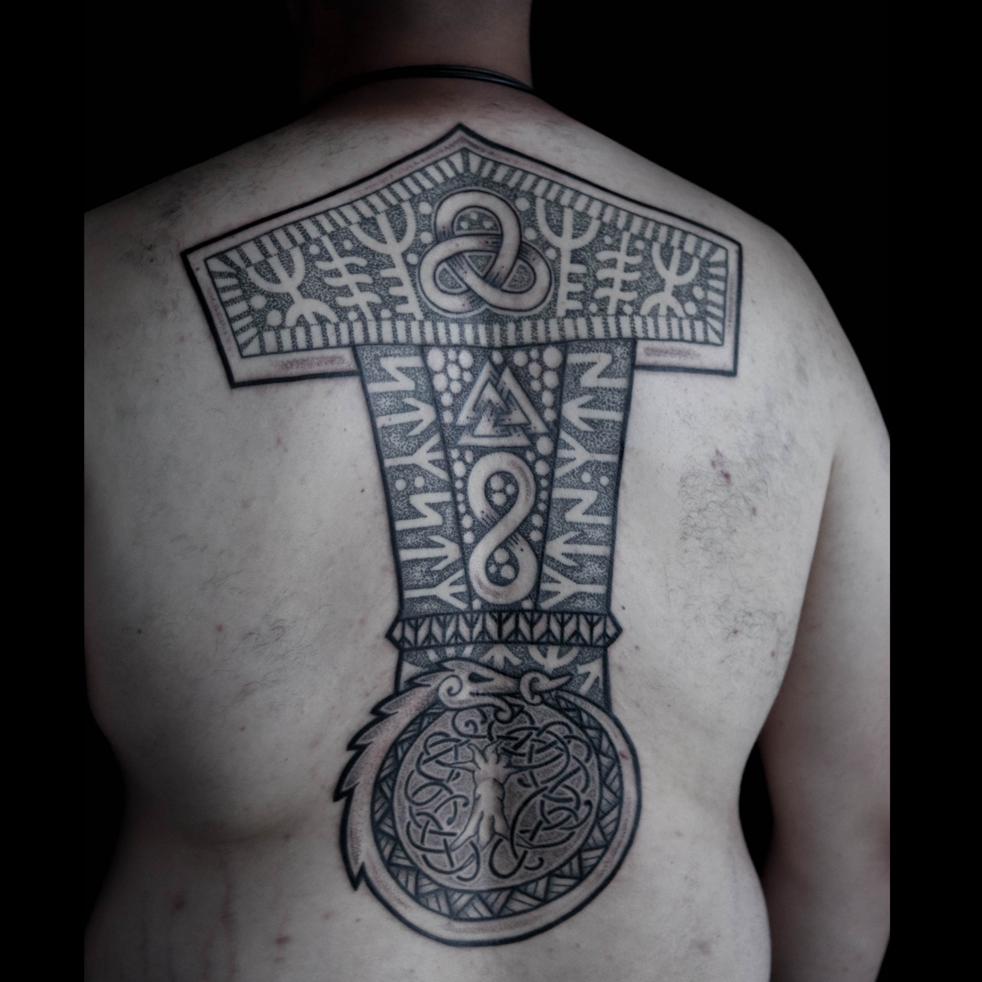 Viking backpiece tattoo featuring a large Mjolnir with bindrunes, a Valknut and Jormungandr with subtle ornamental detailing