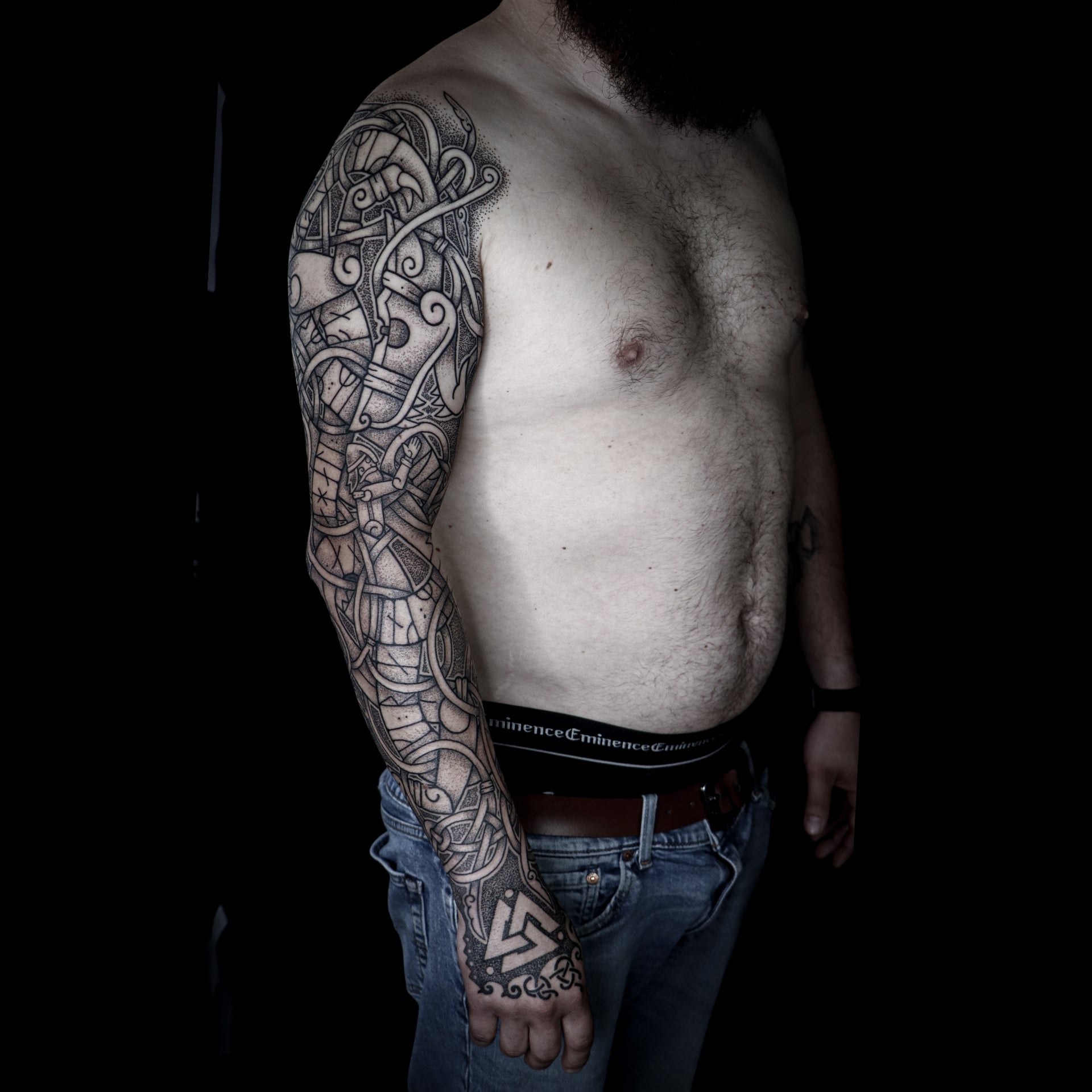 Viking full sleeve tattoo depicting the sacrifice of Tyr with Fenrir across the arm, Valknut on the hand and Younger Futhark runic stanza from the Edda woven into interlaced knotwork design